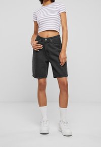 Pantalones cortos de mezclilla negros de cintura alta, con bolsillos frontales y cierre de botón, combinados con una blusa corta a rayas morada y blanca.