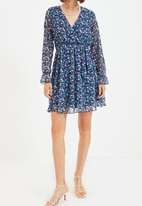 Kukkaprintilla varustettu tummansinisestä kankaasta valmistettu mekko, jossa on pitkät hihat, röyhelöhelma ja istuva vyö. Kangas on läpinäkyvää, pehmeää ja kevyttä.