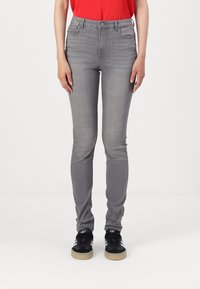 Jeans skinny grises con una textura suave, cintura de altura media, diseño de cinco bolsillos, y combinados con zapatillas negras con rayas blancas.