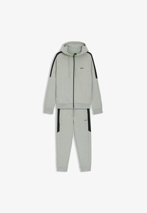 Harmaa huppari ja verkkarit, joissa mustia yksityiskohtia, pehmeä kangas, vetoketjulla avattava etuosa, nyörillä säädettävä huppu ja logo yksityiskohtana rinnassa ja lahkeessa.