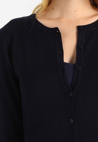 Navyblauer Cardigan aus weichem Stoff mit runder Ausschnitt, Knopfverschluss und langen Ärmeln mit glatter Textur.