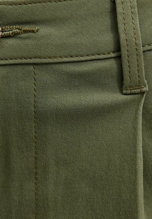 Zbliżenie na oliwkowozieloną tkaninę z pętelką na pasek i widocznym przeszyciem na parze spodni.