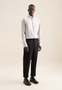 Lichtgrijze button-down shirt met een zak, gecombineerd met zwarte geplooide broeken en zwarte schoenen, tegen een neutrale achtergrond.