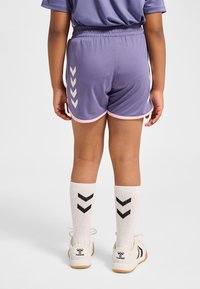 Lila sportshorts med vit kant och chevrondesign. Matchas med vita strumpor med svarta chevroner och vita sportskor.