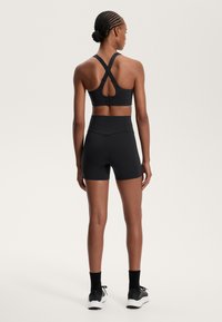 Črna športna modrc s prečnimi naramnicami in obliko ključavnice na hrbtni strani, v kombinaciji z črnimi hlačami z visokim pasom. Gladka tekstura, prilegajoča se zasnova.