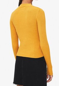 Un pull jaune moutarde à manches longues et à côtes avec une coupe cintrée, contrastant avec une jupe en denim noir et courte. La texture est lisse et extensible.