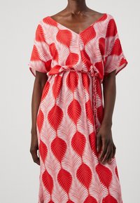 Robe maxi rouge et blanche à motif feuilles, décolleté en V, manches amples et taille froncée avec lien ajustable. Tissu doux et léger.