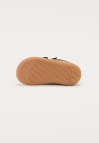 Suela de zapato con una superficie de goma texturizada en tono marrón, que presenta surcos para agarre y marcas de dedo distintivas para mayor tracción.