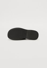 Talpă de pantof neagră, prezentând o suprafață texturată pentru aderență, formă rotundă și două secțiuni distincte din cauciuc. Margini netede și design plat.