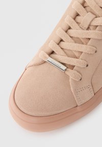 Sneakers Calvin Klein in suede rosa chiaro con lacci piatti, accentuazione in metallo e suola in gomma abbinata; texture liscia e punta arrotondata.