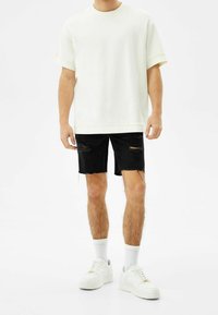 Bílý bavlněný tričko s krátkými rukávy, doplněné černými roztrhanými denimovými šortkami. Bílé tenisky s texturovanou podrážkou a ponožky do kotníků.