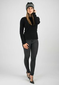Black long-sleeve sweater, black skinny jeans, and pointed black high heels. The model wears a black and white patterned beanie on her head.
