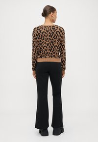 Leopardprint trui in bruin en zwart, geribbelde manchetten en zoom, gecombineerd met zwarte flared broek en dikke zwarte schoenen.