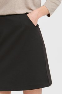 Čierna sukňa vyrobená z hladkej látky, s priliehavým pásom a bočnými vreckami. Lem je rovný a má čistý, minimalistický dizajn.