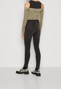 Jeans negros ajustados con cintura alta, con una textura suave y bolsillos traseros, combinados con una blusa de manga larga de oliva con textura de canalé.