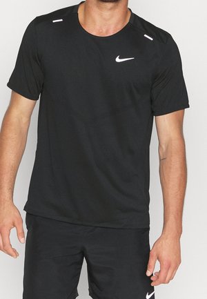 Homme portant un t-shirt de sport Nike noir à manches courtes et un short assorti, debout devant un fond clair uni.