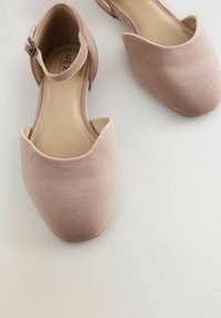 Flache Schuhe aus weichem rosa Wildleder mit einem niedrigen Absatz, mandelförmiger Spitze und einem Knöchelriemen mit einer kleinen metallischen Schnalle.