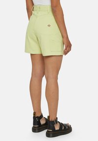 Lys grønne bomullsshorts med høy midje, sidelommer og en baklommepatch. Kombinert med svarte sandaler med stropper og tykk såle.