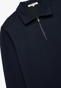 Marineblauwe geribbelde pullover met een staande kraag en halve rits, gemaakt van zachte stof, met textuurdetails en een aansluitend design.