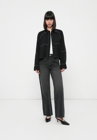 Black cropped jacket with white stitching, paired with high-waisted dark gray jeans. Black high-heeled shoes complete the outfit.