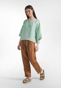 Mintgrøn hørbluse, brune teksturerede bukser med vide ben og olivengrønne sandaler med to spænder. Enkelt design og afslappet pasform.