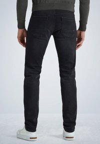 Vaqueros de mezclilla negros con un corte ajustado, dos bolsillos traseros y costuras sutiles. Combinados con zapatillas blancas y un suéter verde.