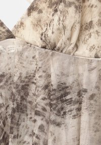 Gros plan sur un tissu beige et marron à motifs avec une superposition en maille montrant des détails froncés et plissés.