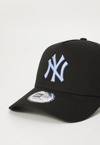 Boné preto de beisebol com uma faixa ajustável, apresentando um logótipo bordado azul claro na frente e uma etiqueta circular da marca na aba.