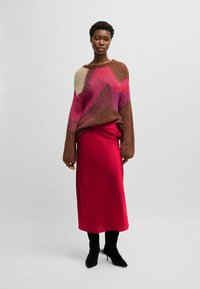Knitted sweater with a zigzag pattern in brown, pink, and cream; paired with a satin red skirt and black heeled boots.