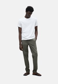 Camiseta de algodón blanca, pantalones oliva y chanclas negras. El ajuste es holgado, con una textura suave y sin patrones ni logotipos visibles.