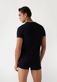 T-shirt nera aderente realizzata in materiale liscio, maniche corte, colletto a girocollo. Indossata con pantaloni corti neri coordinati, mette in mostra una silhouette elegante.