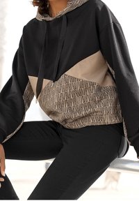 Felpa nera e beige con cappuccio, caratterizzata da un design geometrico e un motivo logo ripetuto. Texture morbida, vestibilità ampia e chiusura con cordoncino.