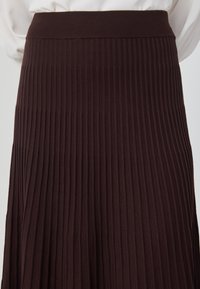 Jupe plissée marron foncé avec une taille côtelée, ornée de rayures verticales, fabriquée en tissu doux et texturé.