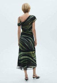 Robe à motifs noirs et verts, coupe ample, décolleté épaules dénudées et longueur mi-mollet. Confectionnée en tissu transparent et léger.