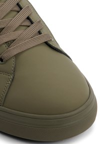 Sneaker verde oliva realizzato in materiale sintetico liscio, punta tonda, suola piatta in gomma e lacci beige. Presenta cuciture sottili e nessun motivo.