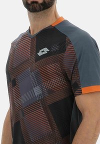 Camiseta deportiva para hombre en gris con patrones geométricos en marrón oscuro y acentos en naranja. Presenta un escote en V y mangas cortas. Material ligero.