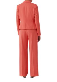 Koraal kleurig pak bestaande uit een getailleerde blazer met een geloperd kraag en wijde pijpen. Glad materiaal en een vakkundig ontwerp voor een verzorgde uitstraling.