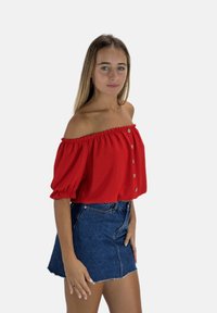 Rode off-shoulder blouse met pofmouwen en knoopdetails, gecombineerd met een blauwe denim mini rok met een rafelige Zoom.