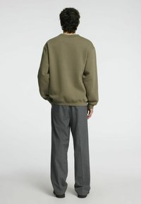 Olivgrön sweatshirt med långa ärmar och rund halsringning, i kombination med grå veckade byxor. Slät textur, avslappnad passform och synlig sömnad.