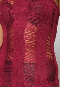 Burgundy stickad topp med öppna vävningar och horisontella samt vertikala ränder, som visar hud genom urklippta sektioner och texturerad tyg.