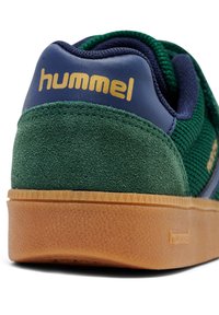 Sneaker in suede verde e mesh blu con suola in gomma color beige. Logo "hummel" dorato vicino al tallone. Dettaglio della superficie testurizzata sulla suola.