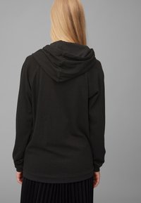 Czarna bluza z kapturem, z podwójnym kapturem, długimi rękawami i luźnym krojem. Gładka faktura z prążkowanym wykończeniem na dole i mankietach.