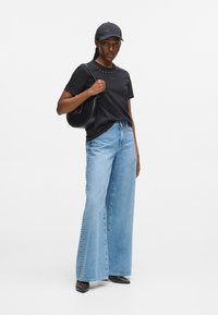 Sort t-shirt med korte ærmer og pyntet halsudskæring, lyseblå vidde bukser, sort håndtaske og sort kasket, kompletteret med dekorative hæle.