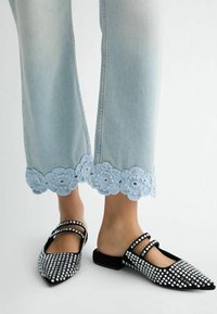 Jean en denim bleu clair avec une finition en crochet de fleurs élaborée au bas, associé à des ballerines noires ornées de clous métalliques argentés et de brides.