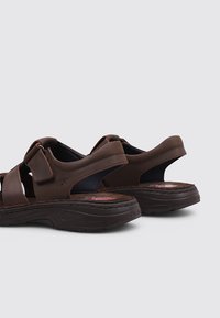 Sandalias de cuero marrón con correas ajustables y suelas acolchadas, que presentan un diseño segmentado y una suela texturizada similar al caucho.