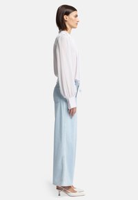 Blusa bianca a maniche lunghe con maniche a sbuffo abbinata a jeans a vita alta azzurri chiari e scarpe con tacco a scomparsa bianche.