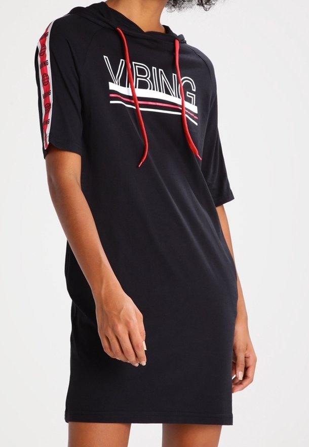 Femme portant une robe à capuche noire à manches courtes avec des cordons rouges, le texte "VIBING" et un motif rayé rouge sur les manches.