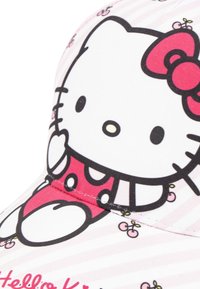 Casquette rose ornée d'un graphique Hello Kitty avec des contours noirs, des motifs à pois et un fond rayé. Détail distinct de nœud en rouge.
