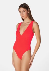 Rode gestructureerde zwemkleding met een diepe V-hals, brede schouderbanden en hoog uitgesneden benen. Het gladde materiaal en het aansluitende ontwerp accentueren de silhouet.