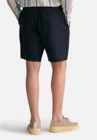 Shorts navy en tissu léger, dotés d'une taille élastique, de deux poches arrière et d'une coupe décontractée. Fini avec une texture lisse.